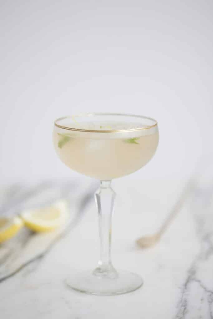 Elegante Clover Gin cocktail in coupeglas met citroen en kruiden op marmeren ondergrond