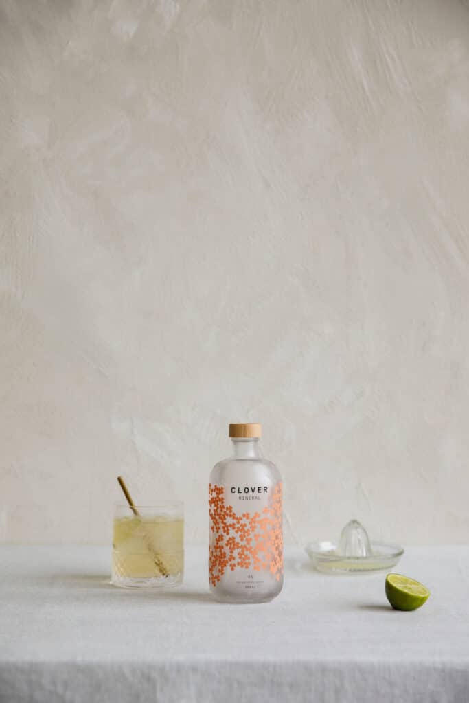 Clover Mineral fles met cocktail en limoen naast citruspers in rustige, minimalistische setting