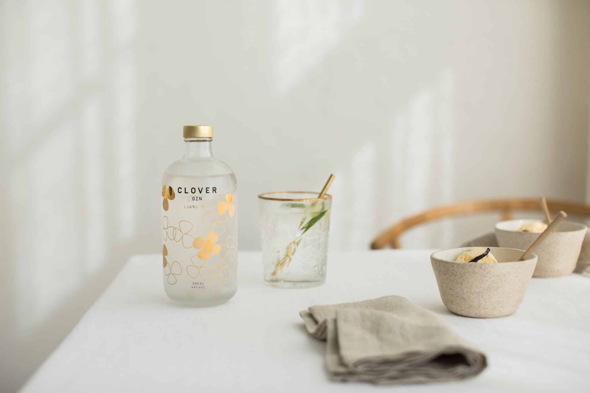 Clover Gin fles op gedekte tafel met glas en botanische garnering in minimalistische setting
